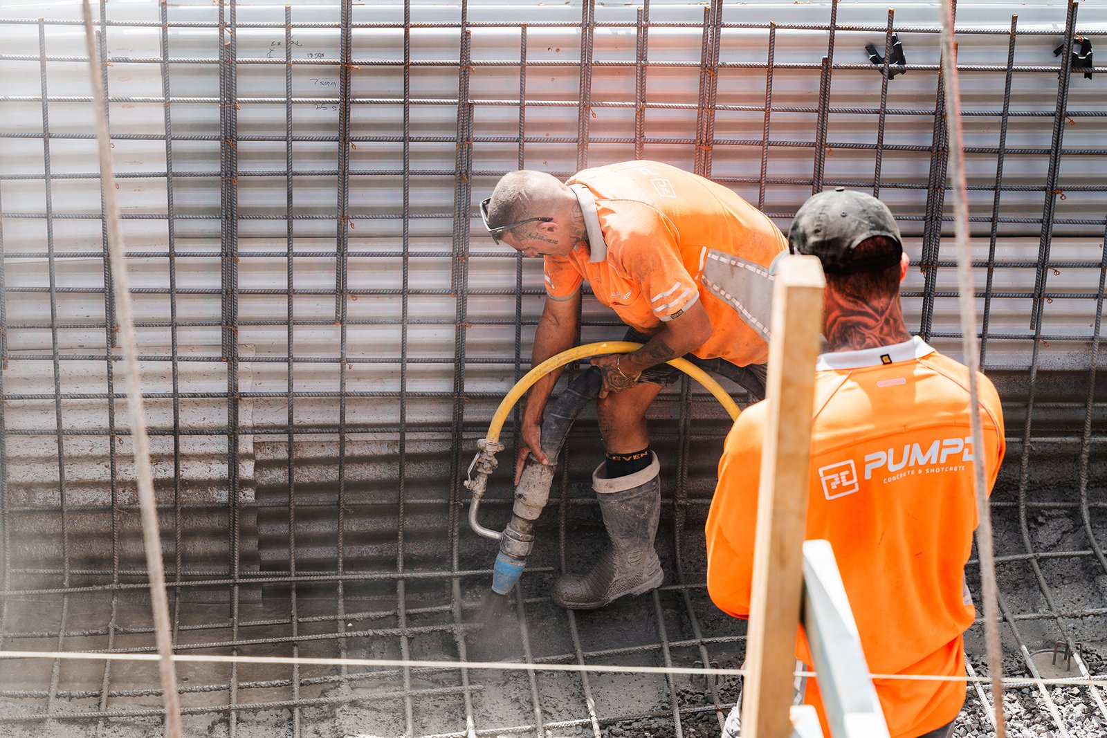 Two Pumpd nozzlemen spraying wet-mix shotcrete onto a reinforced retaining wall